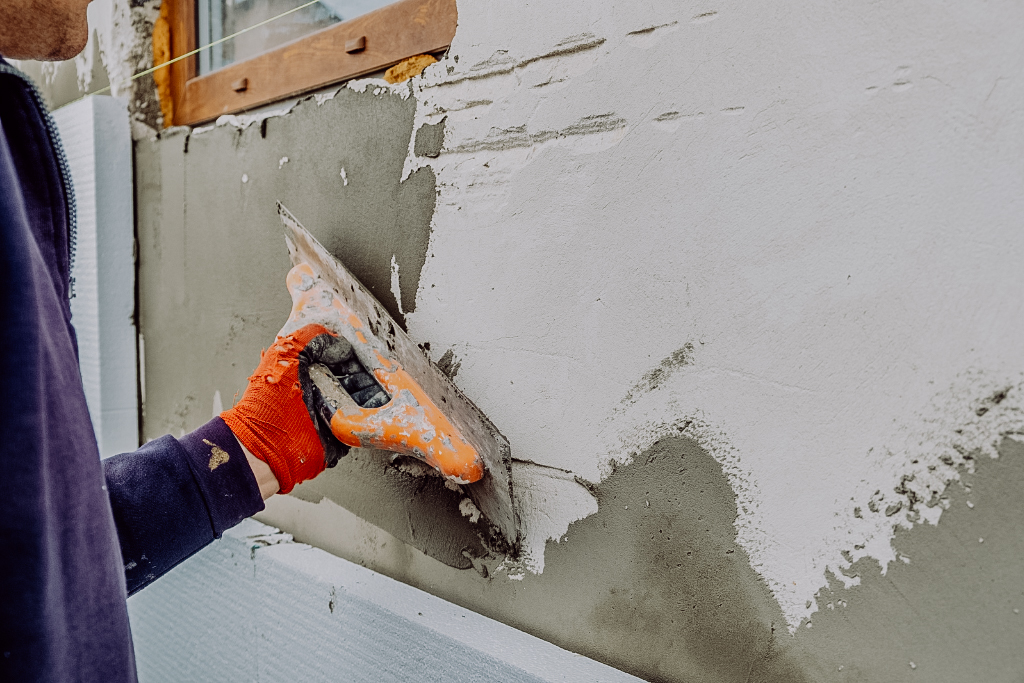 Ein Handwerker trägt Außenputz auf eine Hausfassade auf, zeigt Fachkenntnis und Sorgfalt bei der Außengestaltung.